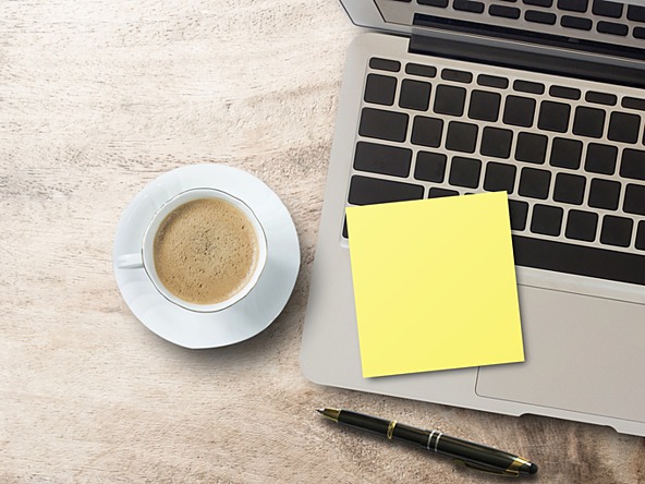 laptop, post-it note, coffee and pen laid on desk